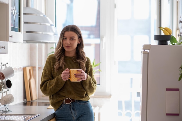 Mujer de pie en la cocina y bebiendo una taza de té