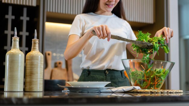 mujer de pie en la cocina y haciendo un plato de ensalada verde