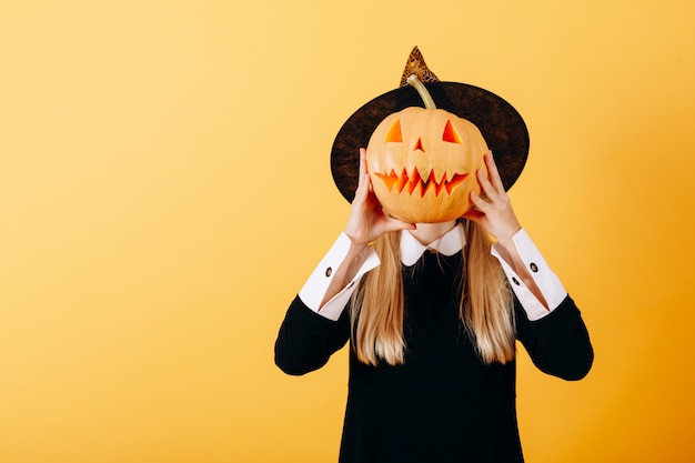 Mujer de pie contra una calabaza amarilla sosteniendo y ocultando su rostro