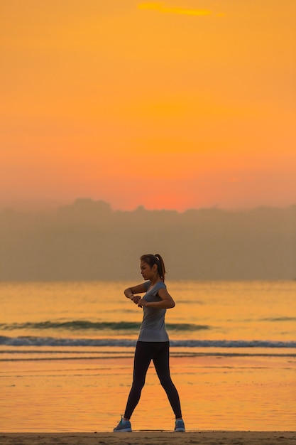 Mujer de pie y ejercicio en beanch por la mañana con cielo colorido y onda de fondo.