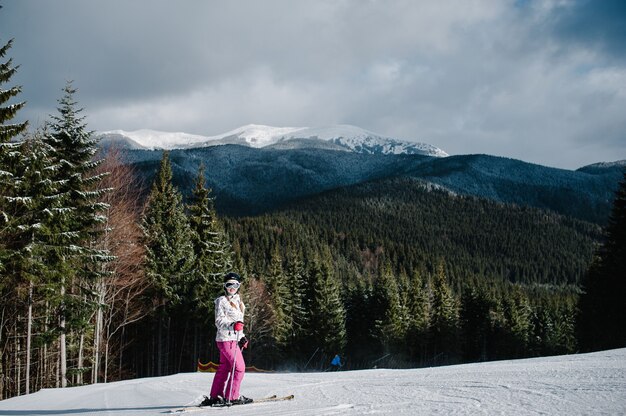 Mujer de pie esquiando, se prepara para descender por la pista de nieve en las montañas de los Cárpatos. En bosque de fondo y pistas de esquí.