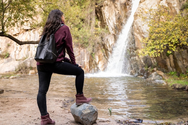 Mujer de pie frente a una pequeña cascada en el bosque