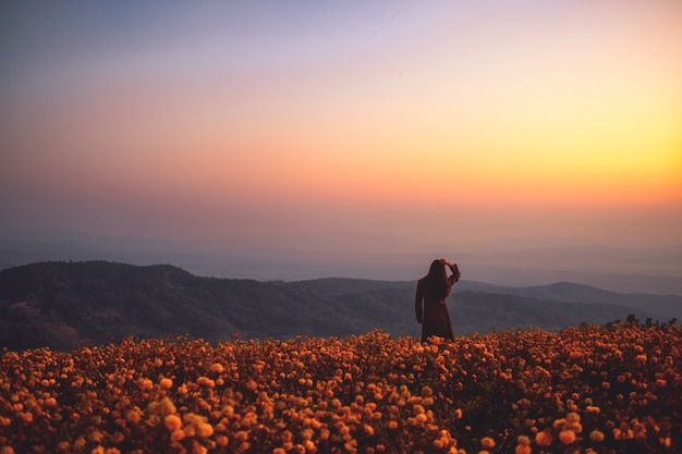 Una mujer de pie entre un hermoso jardín de flores en la cima de la colina antes del amanecer