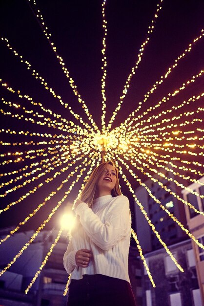 Foto mujer de pie junto a las luces de navidad iluminadas por la noche