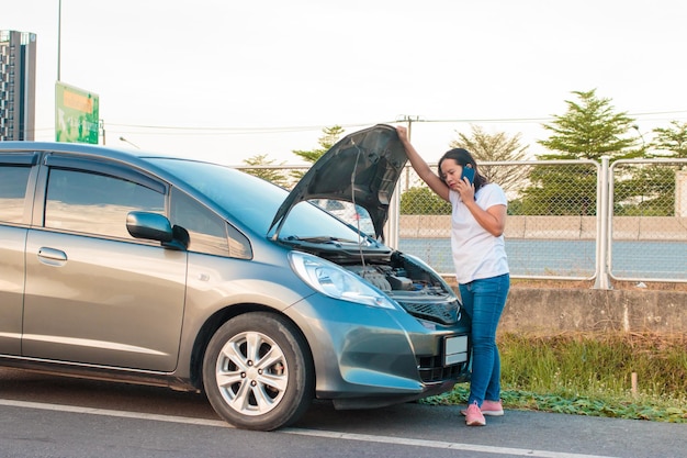 Mujer de pie junto a un vehículo averiado en la carretera de la ciudad