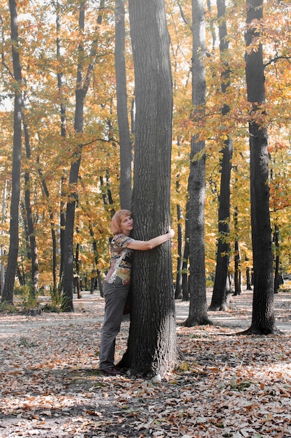 Mujer de pie en medio de los árboles en el bosque durante el otoño y abrazar un árbol