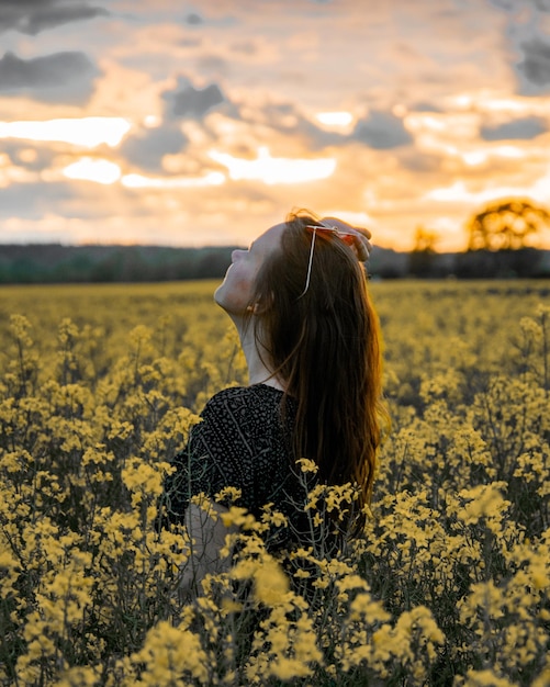 Mujer de pie en medio de flores amarillas en el campo durante la puesta de sol