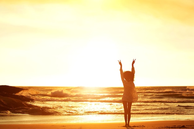 Mujer de pie en la playa con los brazos alzados y signo de la paz