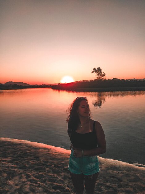 Foto mujer de pie en la playa contra el cielo durante la puesta de sol