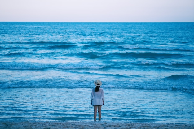 Foto una mujer de pie en la playa, mirando un hermoso mar y un cielo azul solo