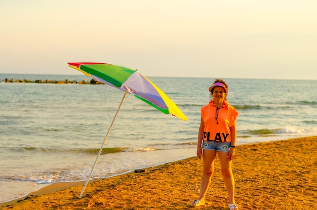 Una mujer de pie en una playa con una sombrilla que dice jugar en ella.