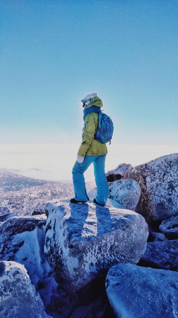 Mujer de pie en una roca contra el cielo azul durante el invierno