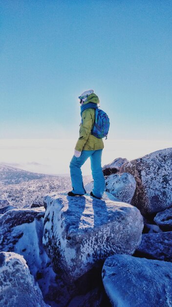 Foto mujer de pie en una roca contra el cielo azul durante el invierno