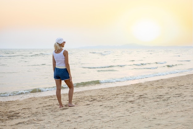 Mujer de pie y viendo el sol en la playa al atardecer