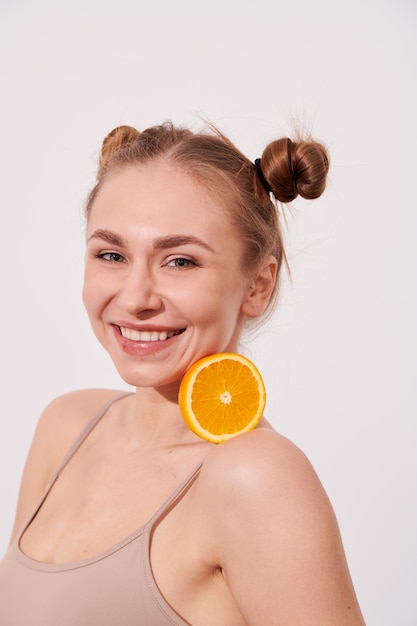 Mujer de piel limpia sonriente feliz sosteniendo naranja cerca de la cara