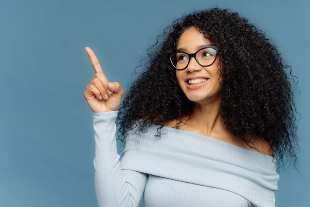 Mujer de piel oscura, sonriente y complacida con puntos de peinado afro con el dedo índice hacia arriba