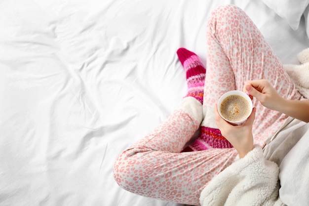 Mujer en pijama sosteniendo una taza de café en su cama