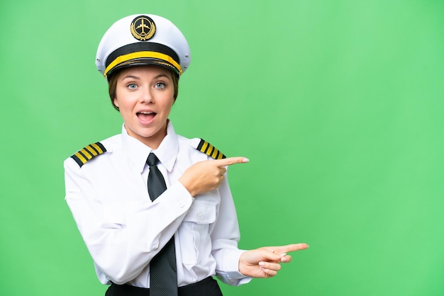Mujer piloto de avión sobre fondo clave de croma aislado sorprendida y apuntando hacia el lado
