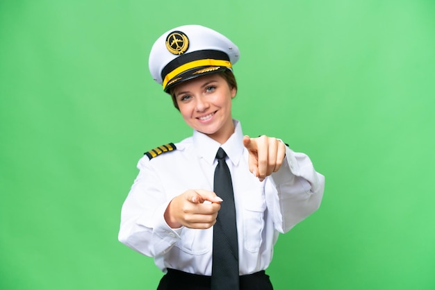 La mujer piloto de avión sobre un fondo de clave de croma aislado te señala con el dedo mientras sonríe