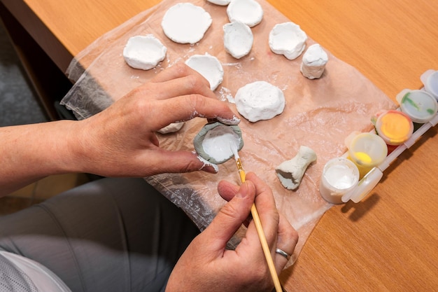 Una mujer pinta un molde de arcilla con pintura blanca. Una clase magistral sobre cómo hacer juguetes de arcilla.