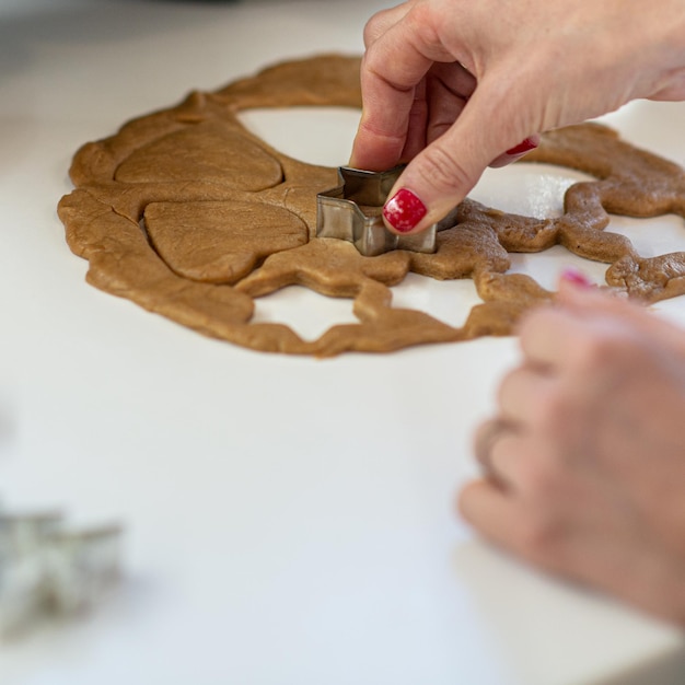 Foto mujer con uñas pintadas de rojo haciendo galletas veganas caseras en forma de estrella y corazón.