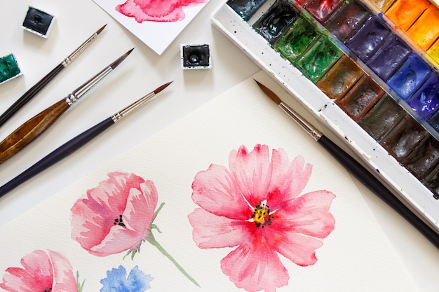 Mujer pintando flores de color rosa con vista superior de acuarelas