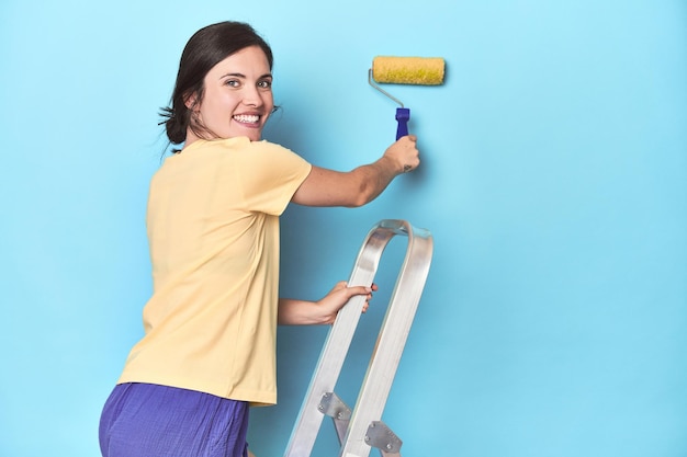 Mujer pintando una pared azul desde una escalera