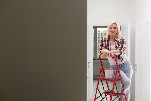 Mujer pintando una pared en un nuevo hogar. Feliz hermosa joven haciendo pintura mural. Una niña hace reparaciones: pinta las paredes con pintura blanca usando un rodillo.