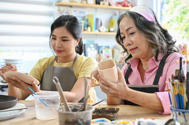 Mujer pintando un plato de cerámica con color acrílico con su abuela en el taller