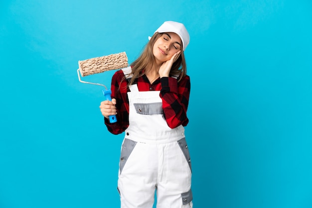 Mujer de pintor sobre fondo azul aislado haciendo gesto de sueño en expresión dorable