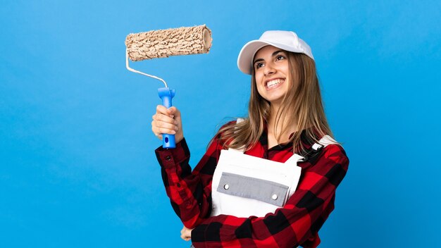 Mujer pintor sobre pared azul aislada apuntando hacia una gran idea