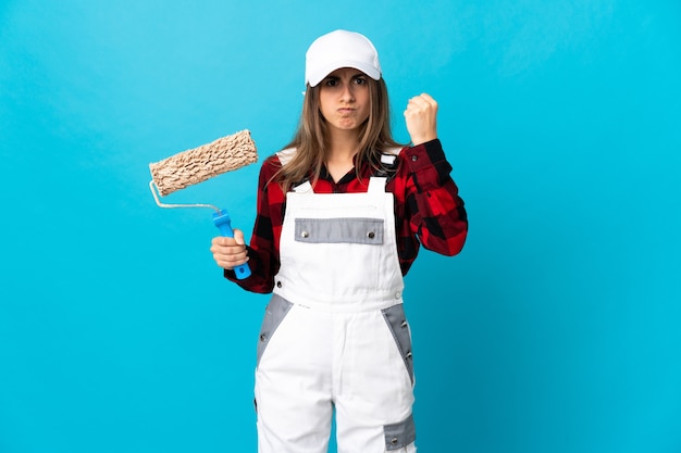 Mujer pintor sobre pared azul aislada con expresión infeliz