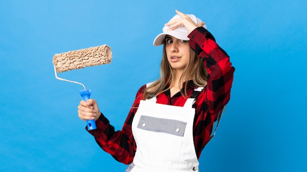 Mujer de pintor sobre pared azul aislada haciendo gesto de sorpresa mientras mira hacia un lado