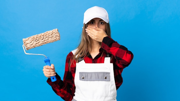 Mujer del pintor sobre la pared azul aislada que cubre la boca con la mano