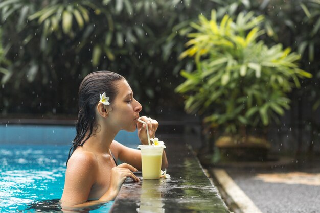 Mujer en la piscina con bebida de frutas