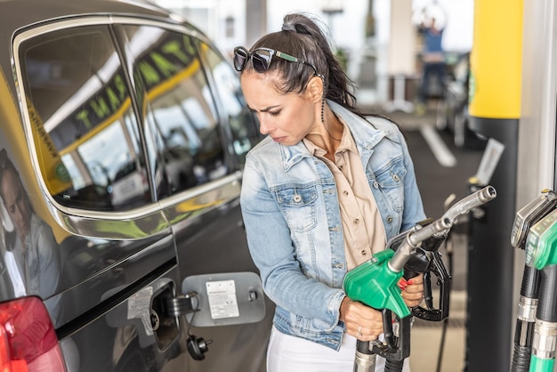 Foto mujer con pistolas de gas y diesel en la gasolinera mira el tanque de gas abierto de su coche