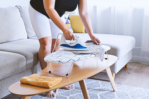 Mujer planchar en una pequeña tabla de planchar en la mesa en la sala de luz, vista lateral