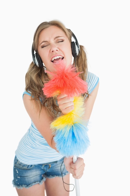 Mujer con plumero como micrófono y escuchar música con auriculares
