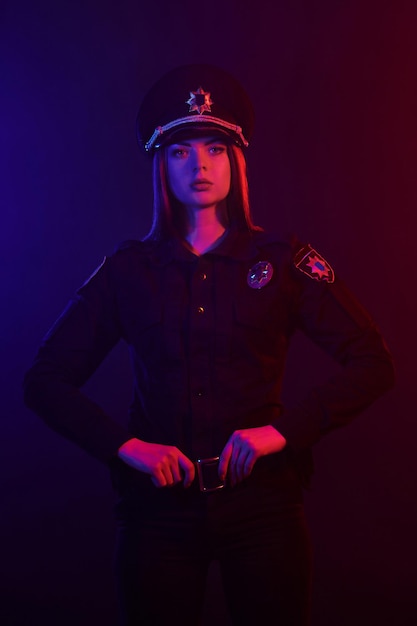 Mujer policía pelirroja está posando para la cámara sobre un fondo negro con rojo y azul ...