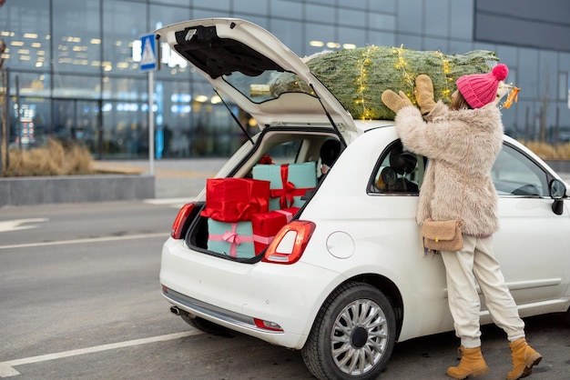 La mujer pone el árbol de navidad en el techo de un auto cerca del centro comercial