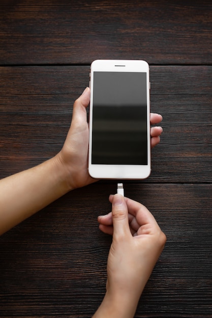 Mujer pone cargando un teléfono blanco sobre una mesa de madera oscura