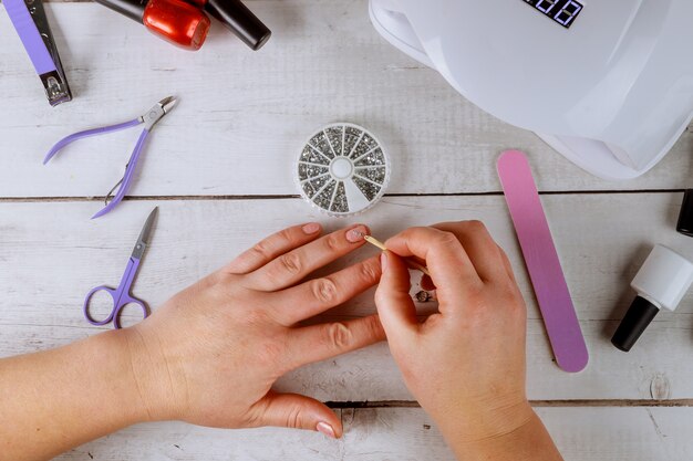 Mujer pone diamantes de imitación en las uñas Fabricación de gel de manicura.