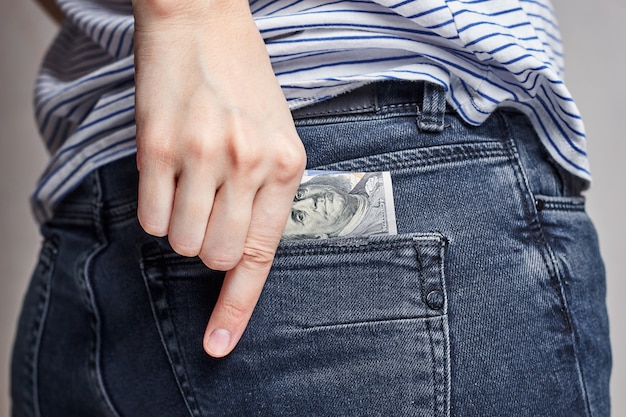 La mujer pone dinero en el bolsillo trasero de un jeans.