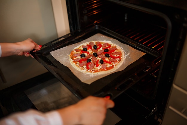 Mujer pone pizza cruda con ingredientes y tomate, especias, salchichas