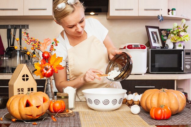 Una mujer pone requesón en masa para galletas para Halloween en la cocina con decoración otoñal. Acogedora casa y preparación, Elaboración de galletas para Halloween.