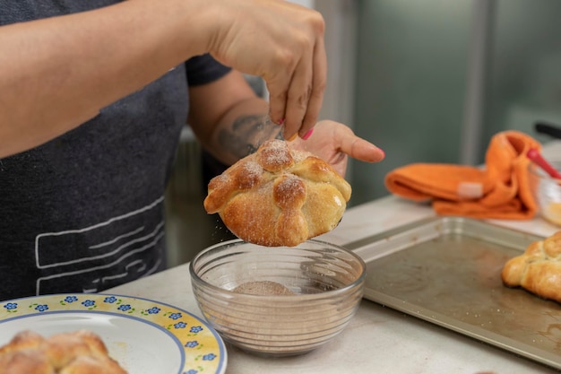 Mujer poniendo azúcar en un pan de muerto recién horneado en casa