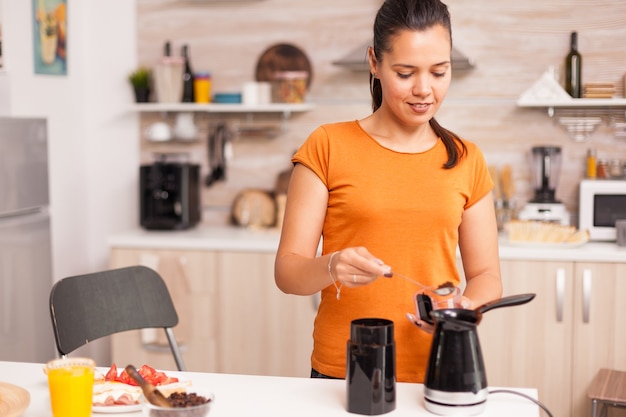 Mujer poniendo café molido en la tetera, en la cocina