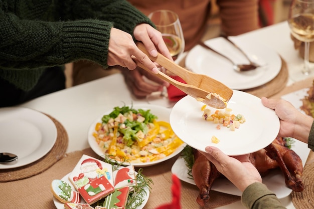 Mujer poniendo ensalada en plato de invitado en la cena familiar de navidad