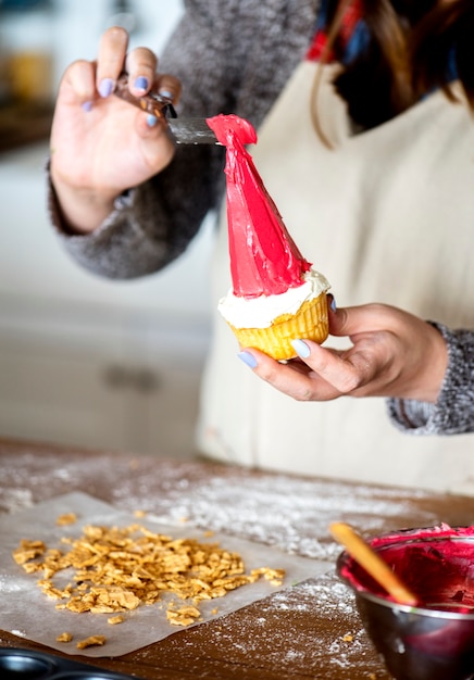 Mujer poniendo glaseado en un cupcake de sombrero de Santa