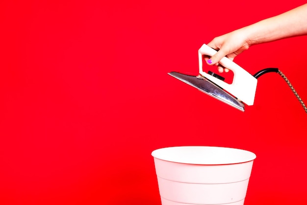 Mujer poniendo hierro en el contenedor de reciclaje sobre fondo rojo